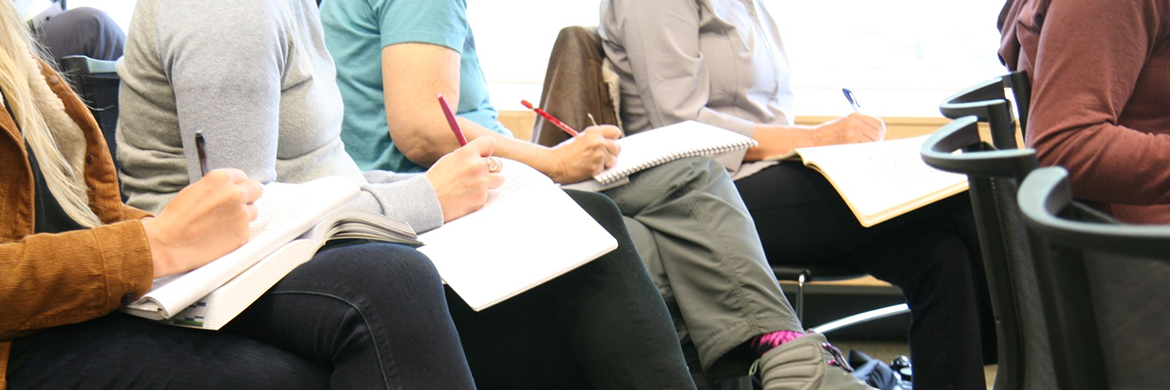 Group of people sitting in chairs and writing with pens and notebooks in their laps