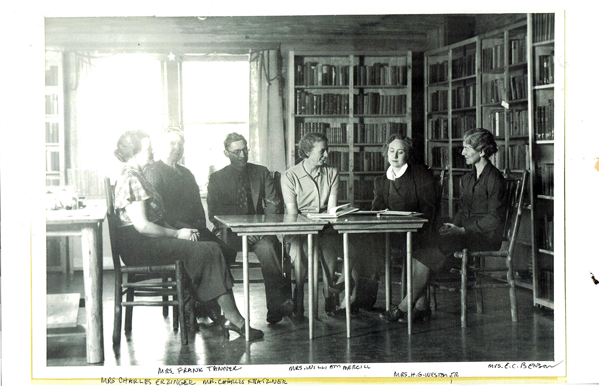 Black and white photo of an early board meeting showing six people (five women and 1 man) sitting at a table in the library