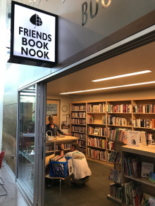 Book Nook entrance with a lighted sign showing the interior where a woman stands at a front desk while a man browses a shelf
