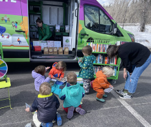 Group of small children with educator outside of the outreach van looking through books