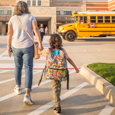 a parent and child hold hands as they walk toward school