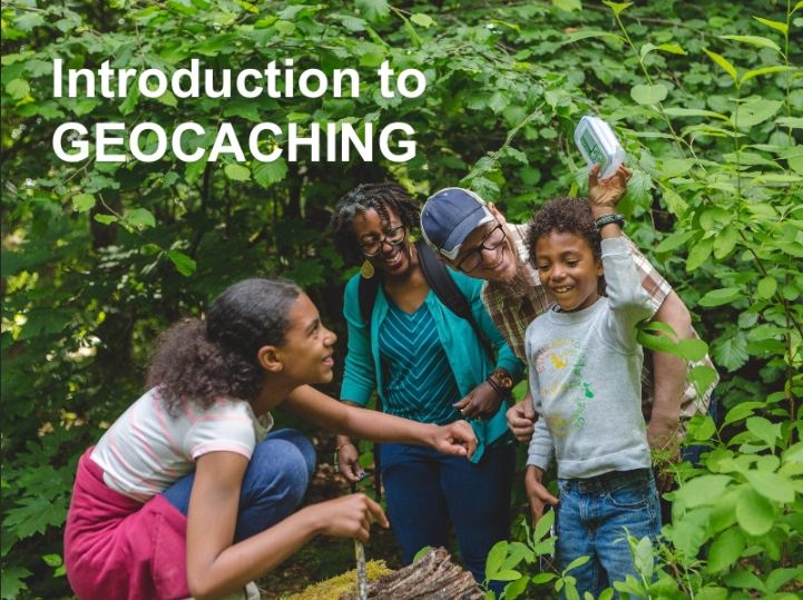 Picture of a group of 4 people outside, a young smiling child has the geocache box in their hand.