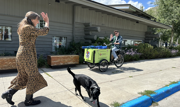 Man riding the book bike and waving at a woman walking her dog