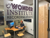 Wonder Institute Recording Studio room with a man sitting at a microphone with headphones on