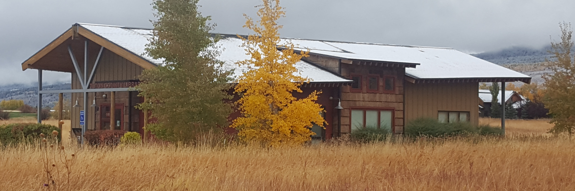 Brown building in the middle of a wheat field with two trees starting to change colors in the fall