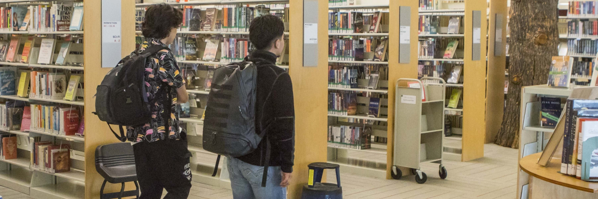 image of teens walking through the library with backpacks on